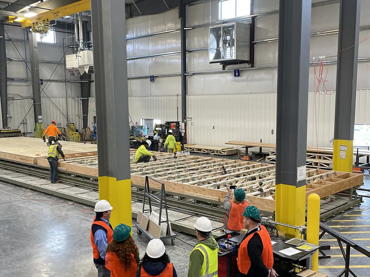 Workers in hard hats and high-visibility vests on the floor of a manufacturing facility.