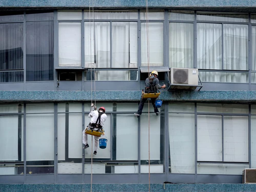 Technicians servicing air-conditioning units mounted on the facade of a building.