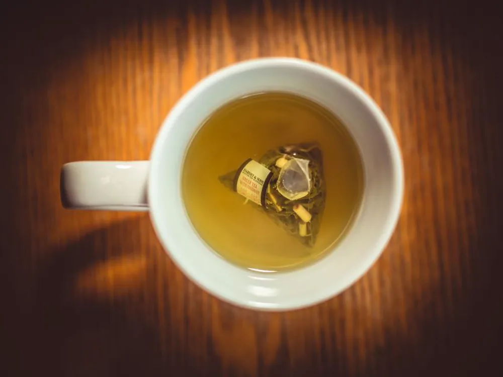 A cup of freshly brewed tea on a warm wooden table, seen from above.